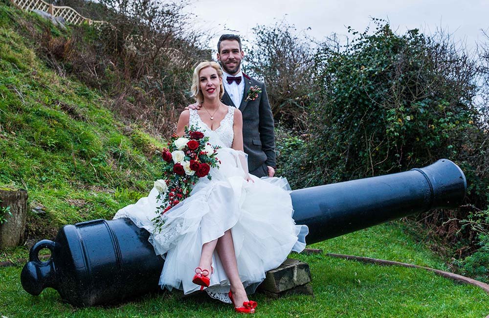 Bride and groom sitting on a cannon at Polhawn Fort Cornwall