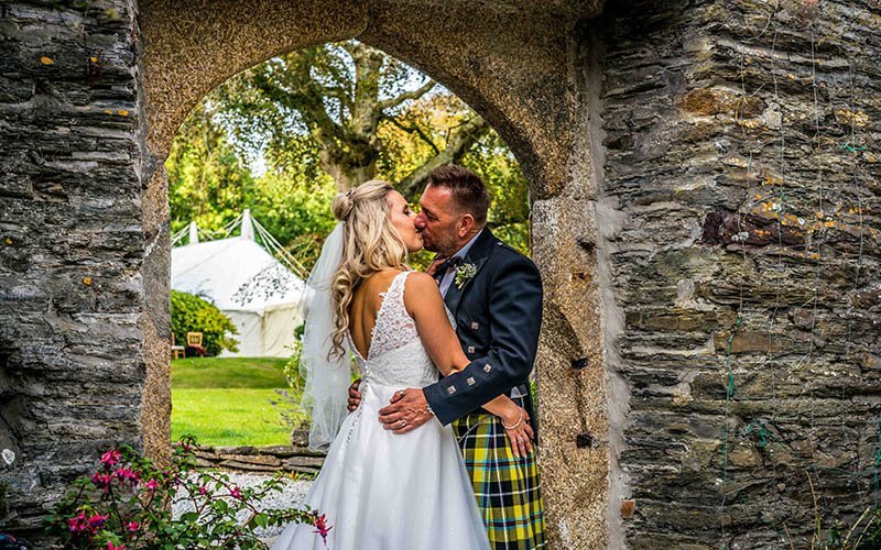 bride and groom kissing under a stone arch