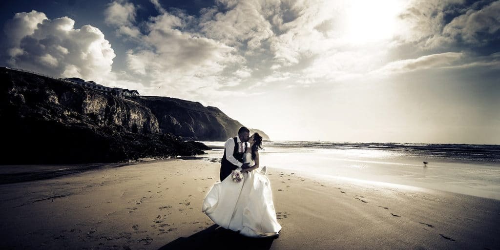 bride and groom kissing on perranporth beach Cornwall sepia