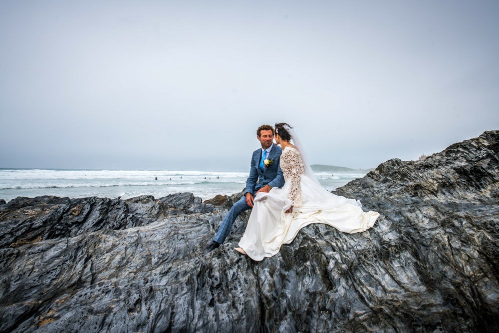 bride and groom sitting on a rock at the beach