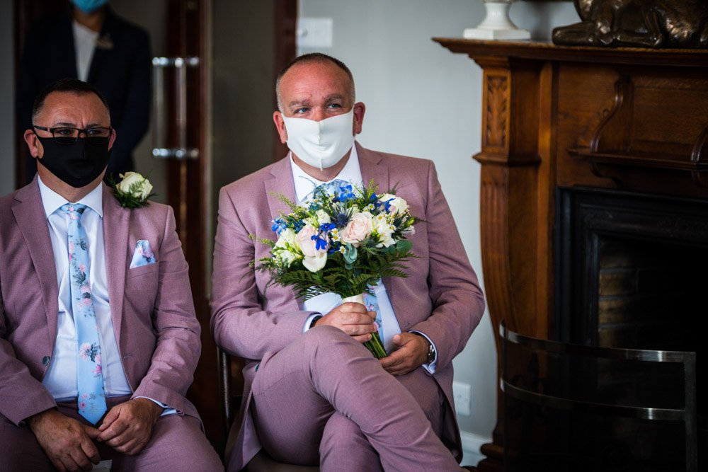 best man in a covid mask holding the brides bouquet at the wedding ceremony