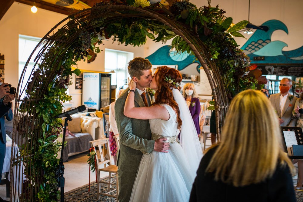 bride and groom kissing under a floral arch