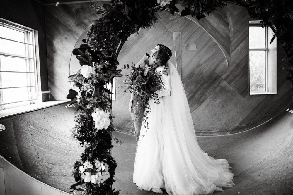 Bride and groom embrace under a floral arch