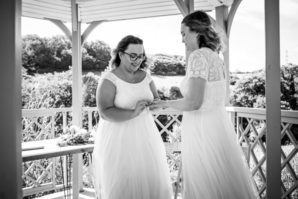 bride and bride exchanging rings at Pengenna Manor Cornwall B&W