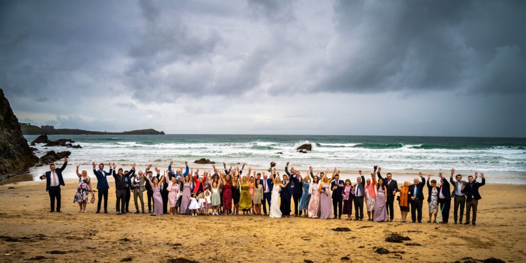 wedding group shot of everyone on the beach waving