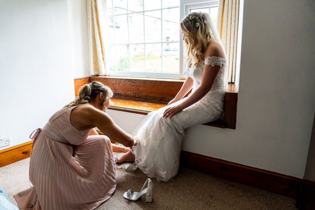 bride having shoes fastened by bridesmaids