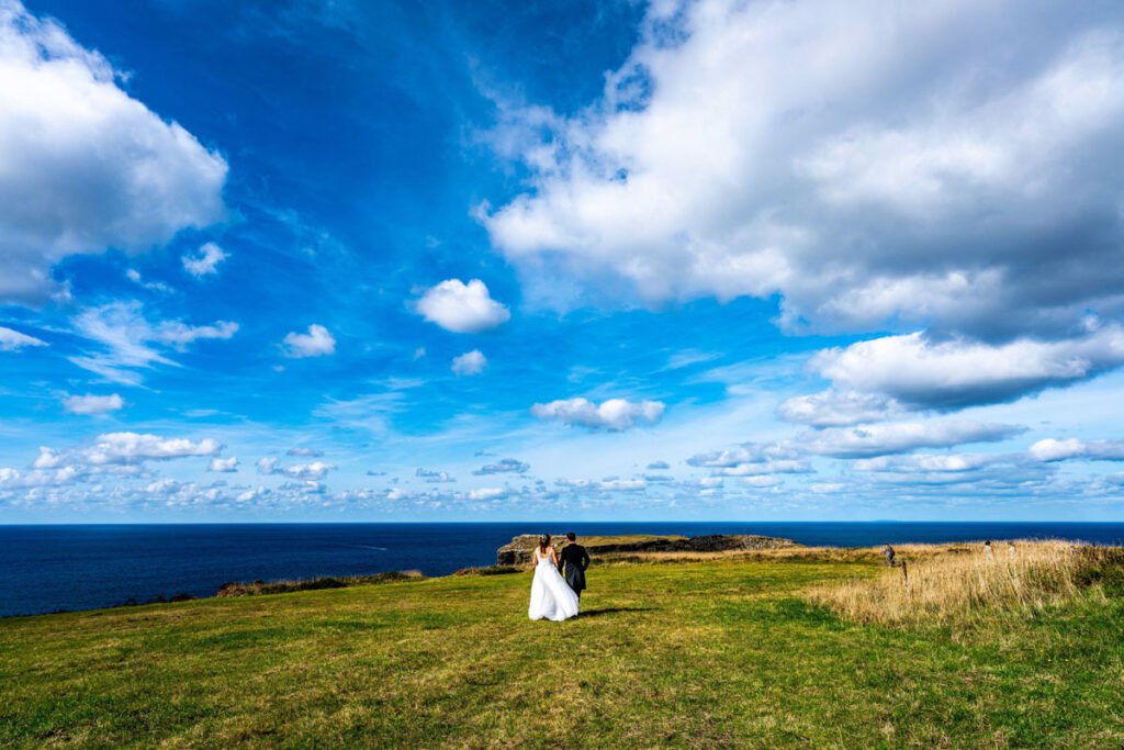 Bride and groom walking away on the cliff overlooking tintagel island