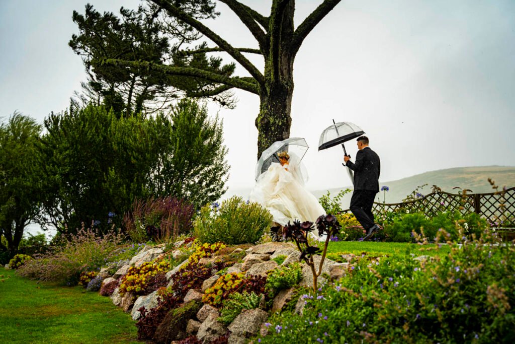 bride and groom with umbrellas in the garden at Polhawn Fort cornwall wedding venue