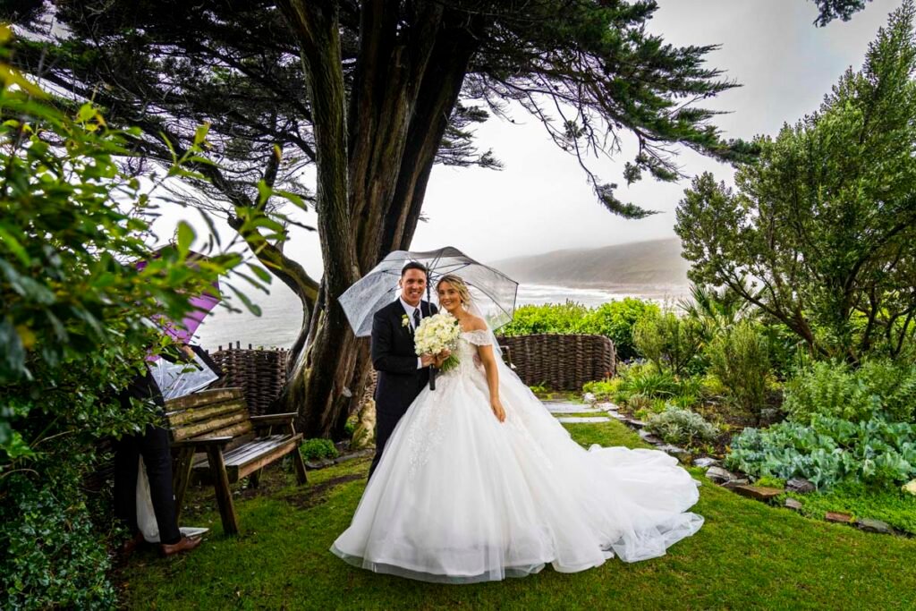 bride and groom with umbrella in the garden at Polhawn Fort cornwall wedding venue