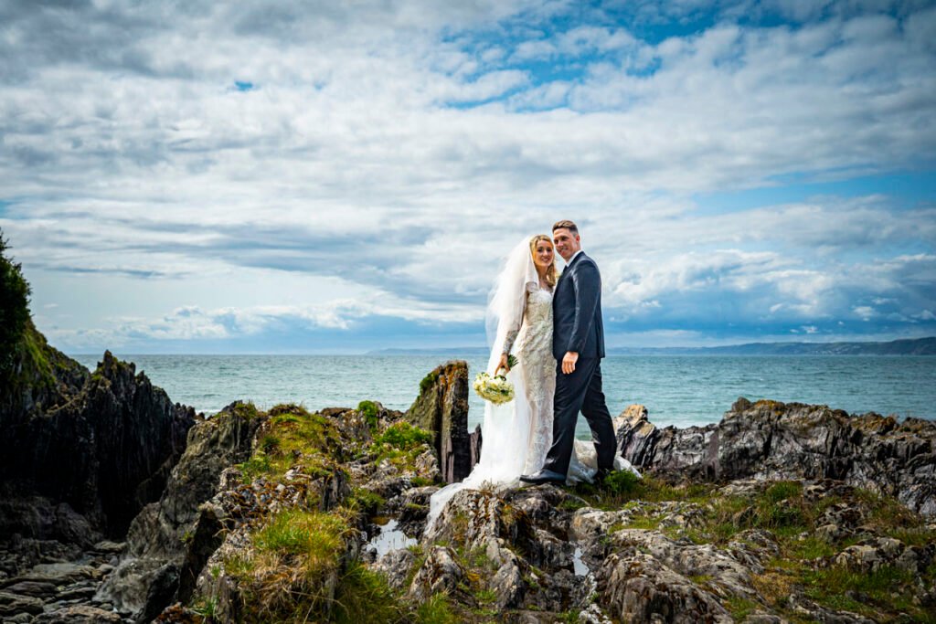 bride and groom stood on a rock at Polhawn fort beach cornwall
