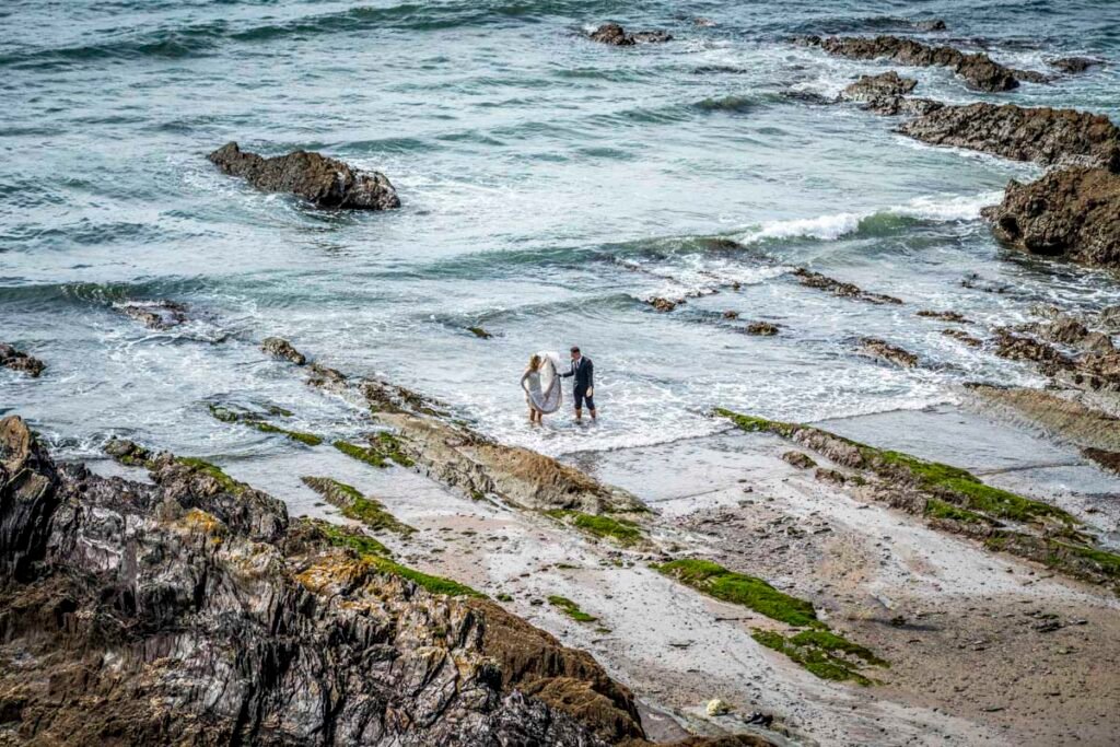 bride and groom paddling in the sea at Polhawn fort cornwall