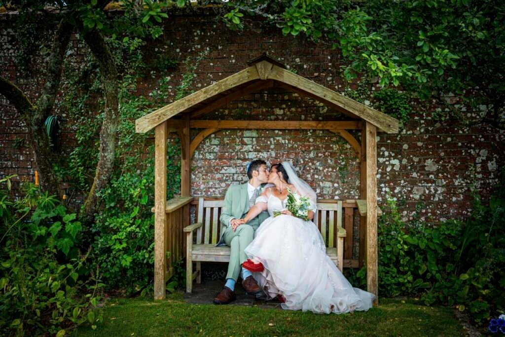 bride and groom kissing on a bench under an arbour