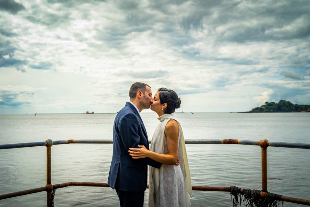 bride and groom embrace overlooking Plymouth Sound