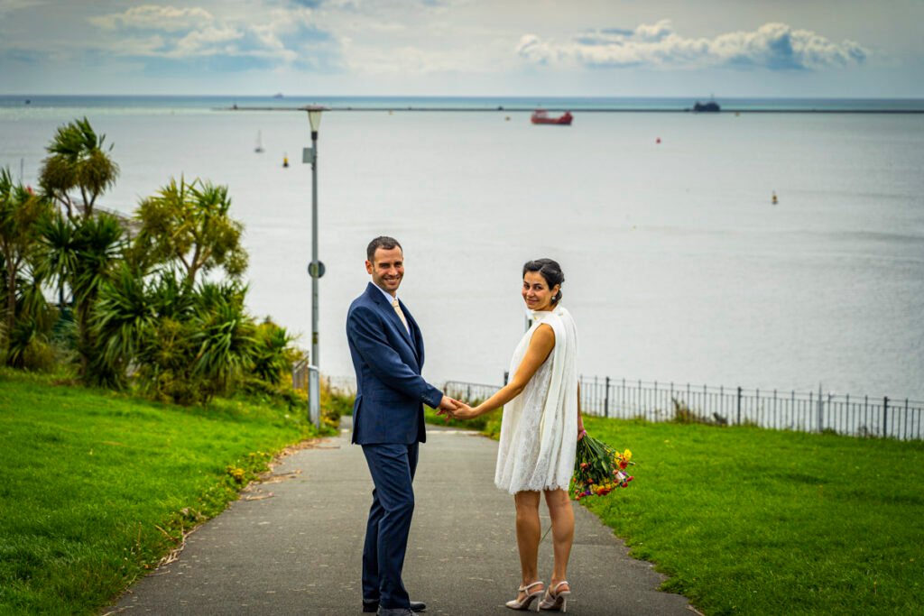 bride and groom holding hands overlooking Plymouth Sound