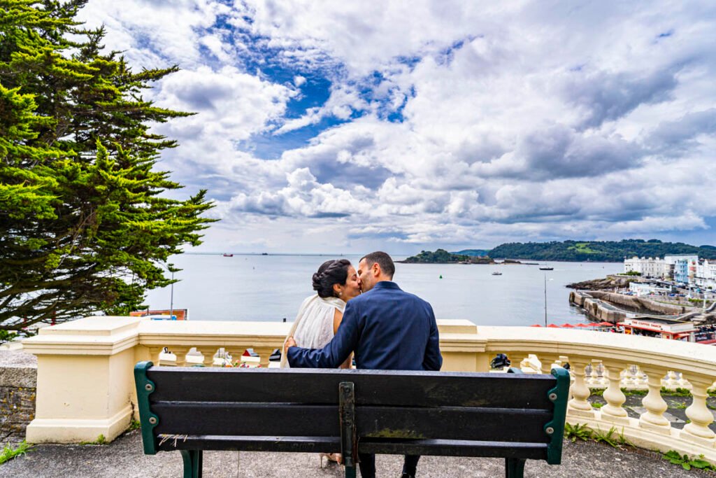 bride and groom kissing on a bench overlooking Plymouth Sound