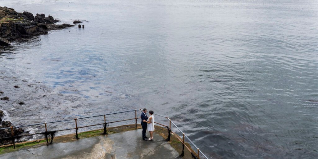 bride and groom embrace overlooking Plymouth Sound