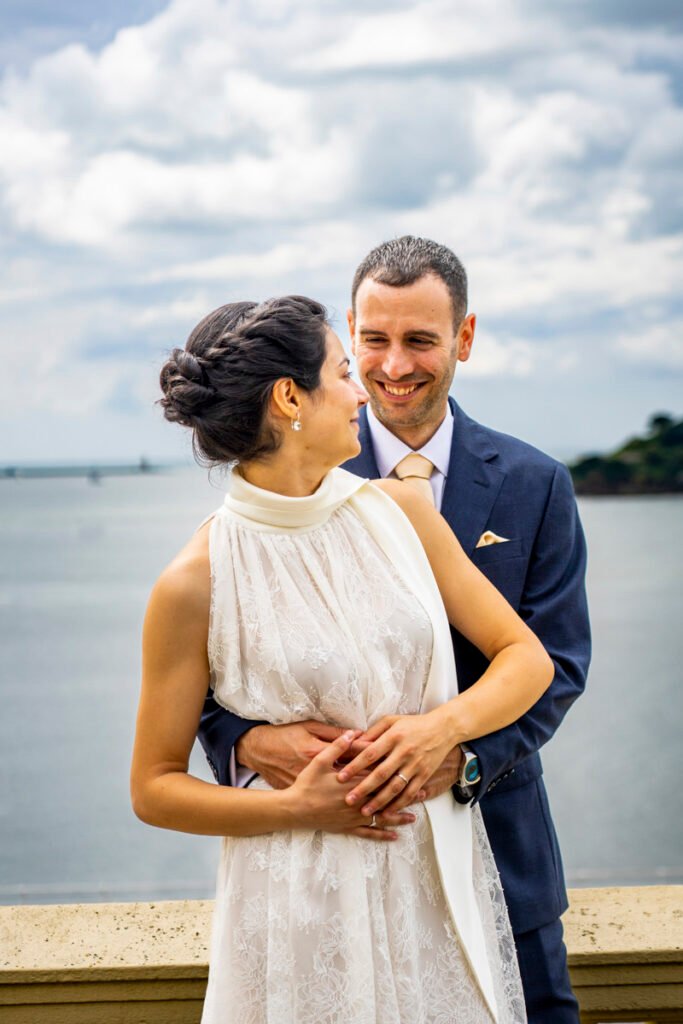 bride and groom embrace overlooking Plymouth Sound