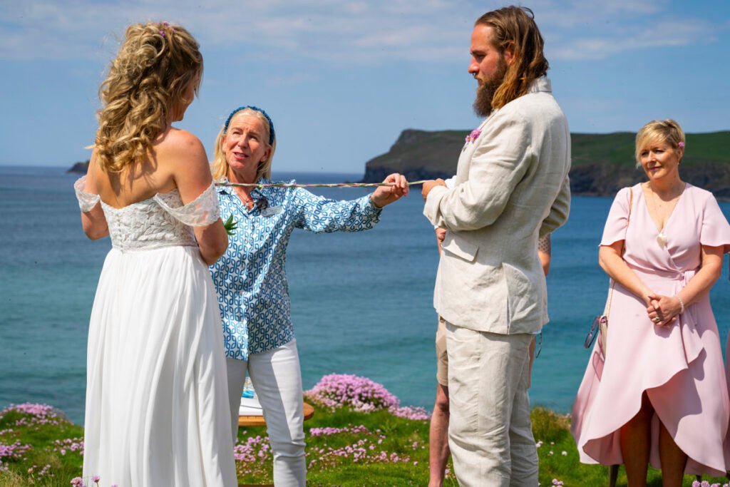 bride and groom tying the knot at the wedding ceremony on the cliff top overlooking the beach